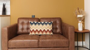 A brown leather sofa with a zigzag patterned cushion against a mustard yellow wall. - The Oasis Apartment (Leeds)