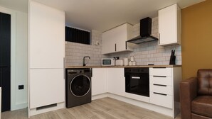 A compact kitchen with a washing machine, microwave, oven, and a coffee maker. - The Oasis Apartment (Leeds)