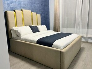 Un llit amb capçalera, roba de llit blanca i una franja decorativa fosca.