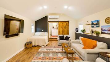 A cozy living room with a sofa, a coffee table, and a TV mounted on the wall. There is a wooden floor and a patterned rug.
