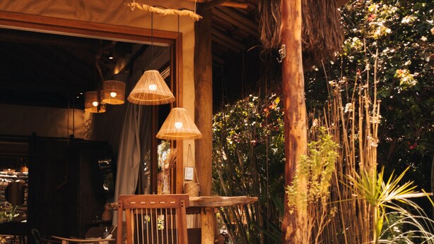 Une terrasse extérieure en bois, agrémentée d’une pergola, de lampes en osier et d’un espace détente avec des chaises et une table.