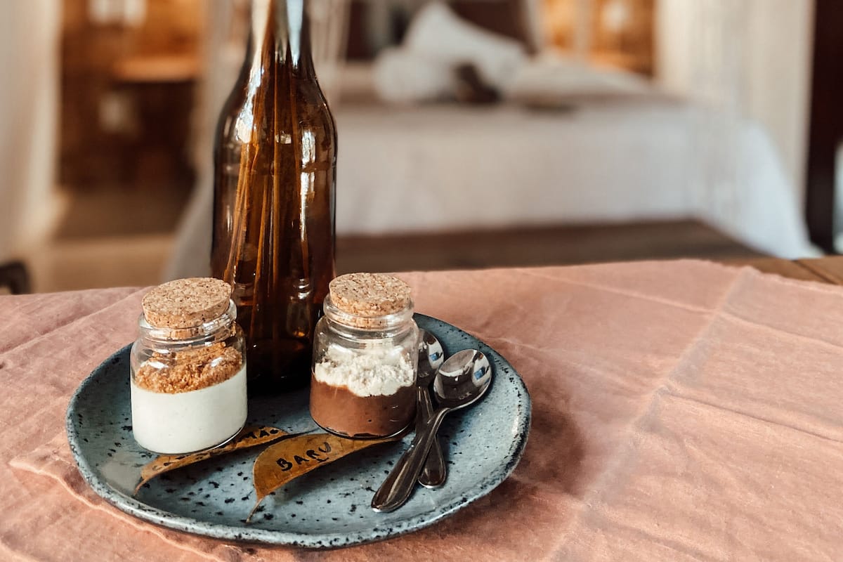 A dessert setup with two jars on a plate, a bottle, and a decorative arrangement of dried flowers and branches.