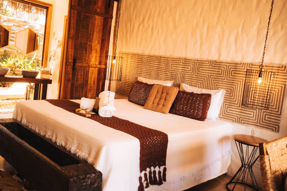 A large bed with a patterned headboard, a wooden bench, and a small table with a chair.