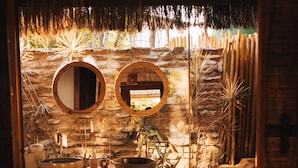 Une salle de bain avec deux miroirs ronds, un lavabo et une fenêtre donnant sur un jardin de rochers naturels.