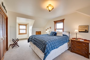 A bedroom with a large bed, a wooden dresser, a nightstand, a wall-mounted lamp, and a window. - Charming Country Home in Laramie - 4 Mi to UW! (Laramie)