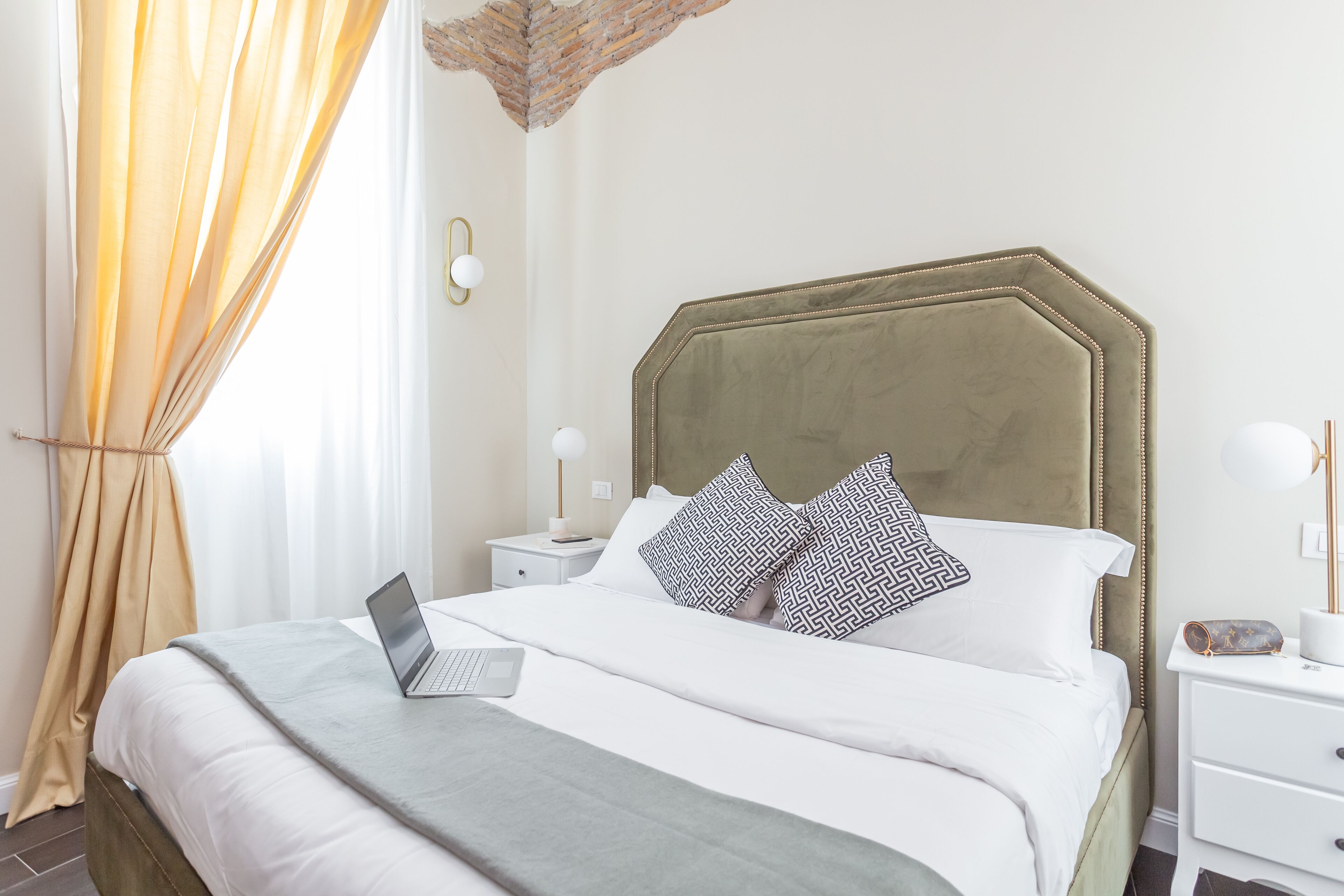 A neatly made bed with a laptop, a bedside table with a lamp, and a nightstand with a lamp.