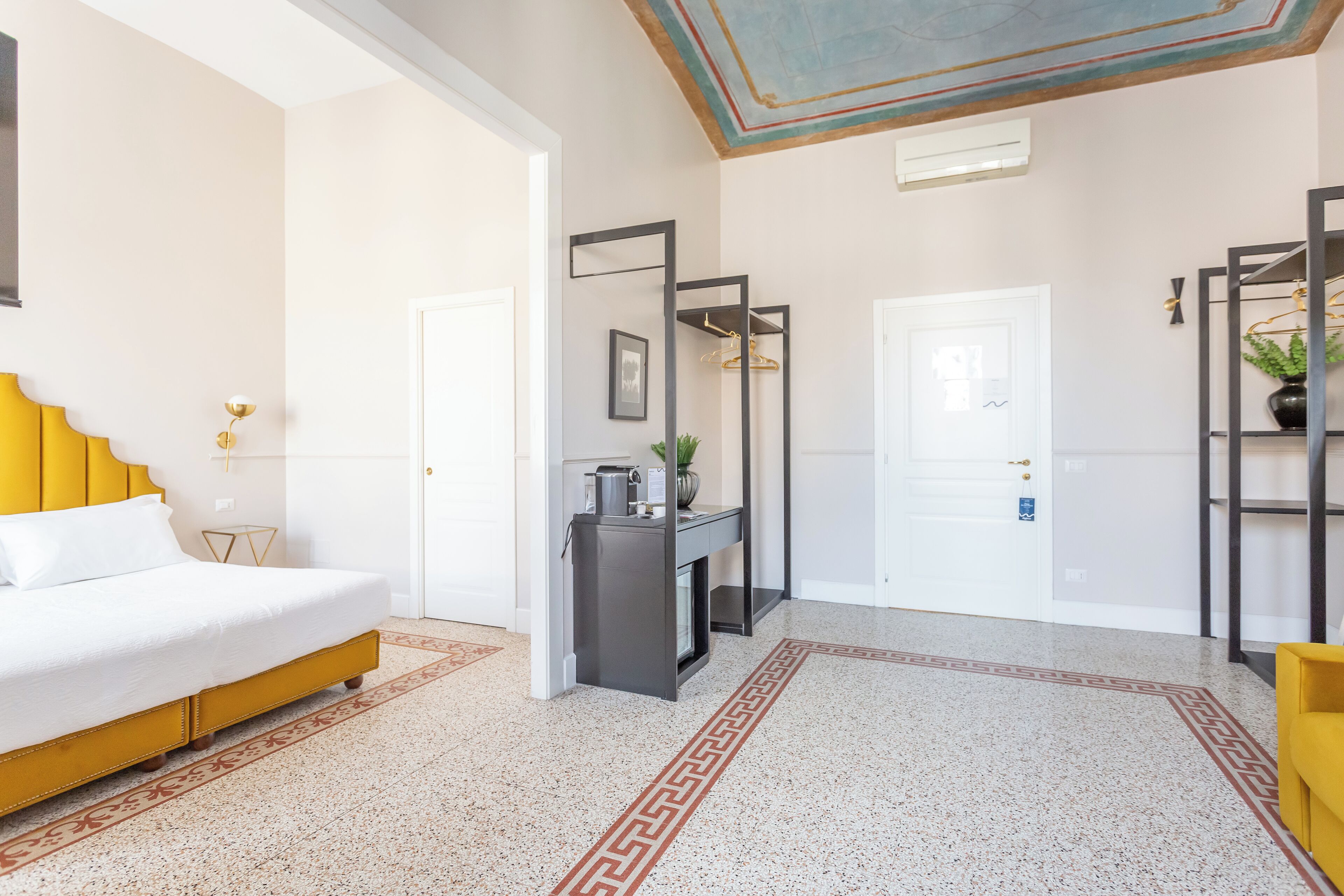 A hotel room with a bed, a desk, a mirror, a coat rack, and a door.