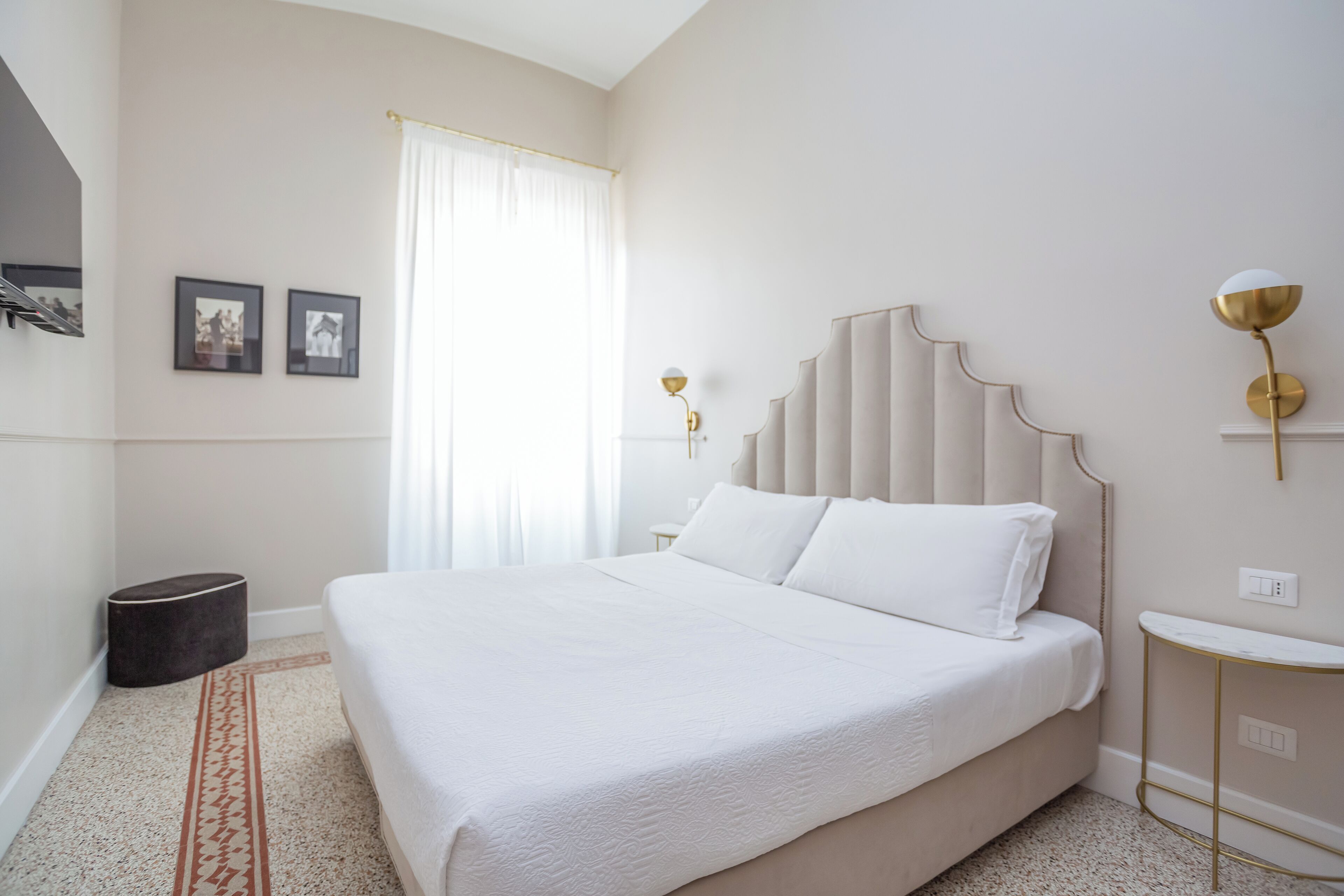 A modern bedroom with a large bed, a bedside table, a lamp, and a small round stool.