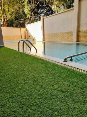 Una piscina con césped artificial, una escalera metálica y un muro de ladrillo.