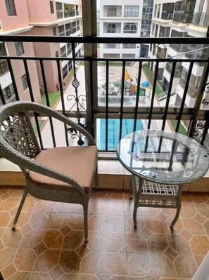 Enjoy the view of the pool and surrounding buildings from this balcony, which features a wicker chair and glass table.