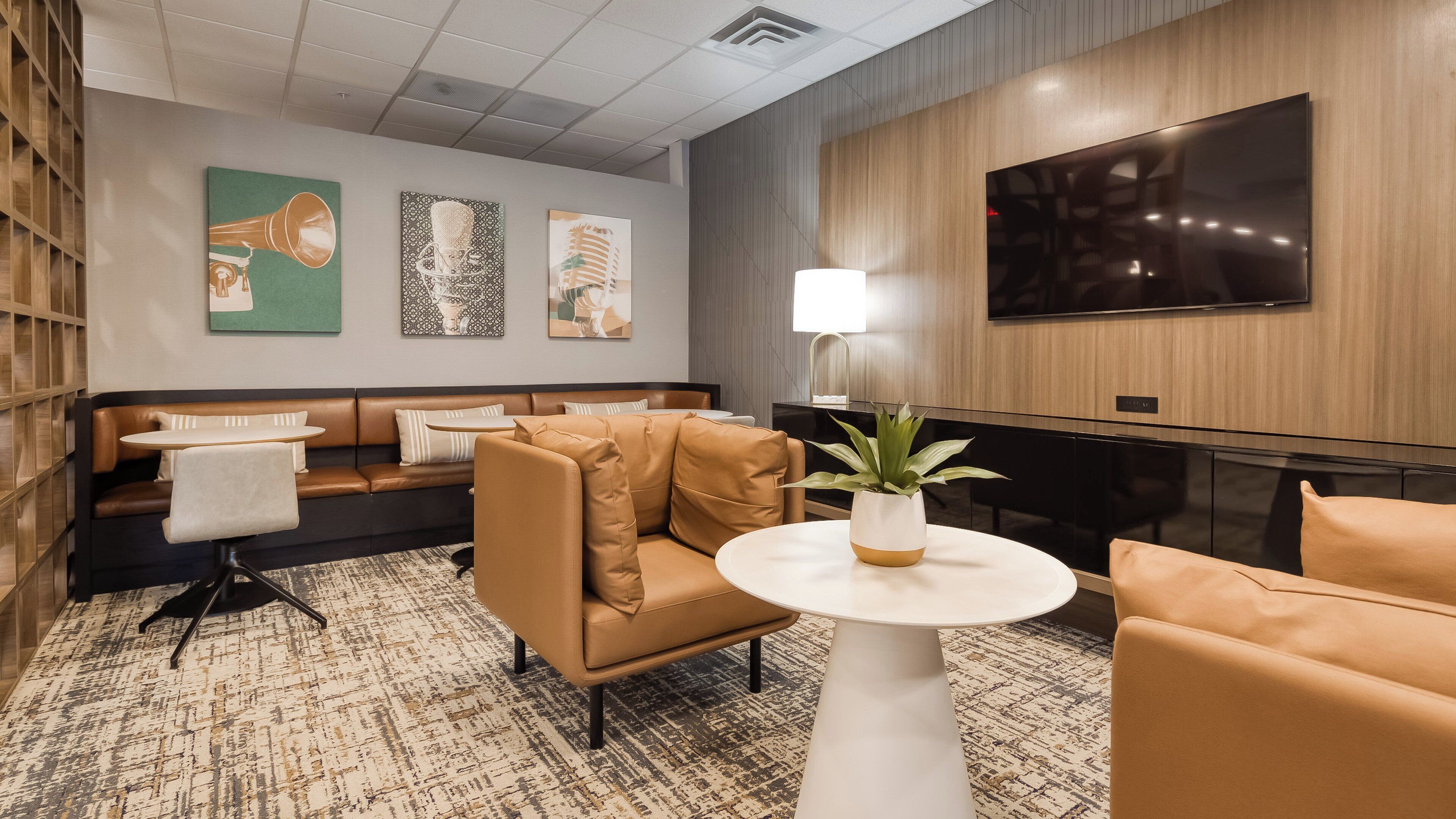 A modern lounge area with leather seating, a round table, and a flat-screen TV mounted on the wall.