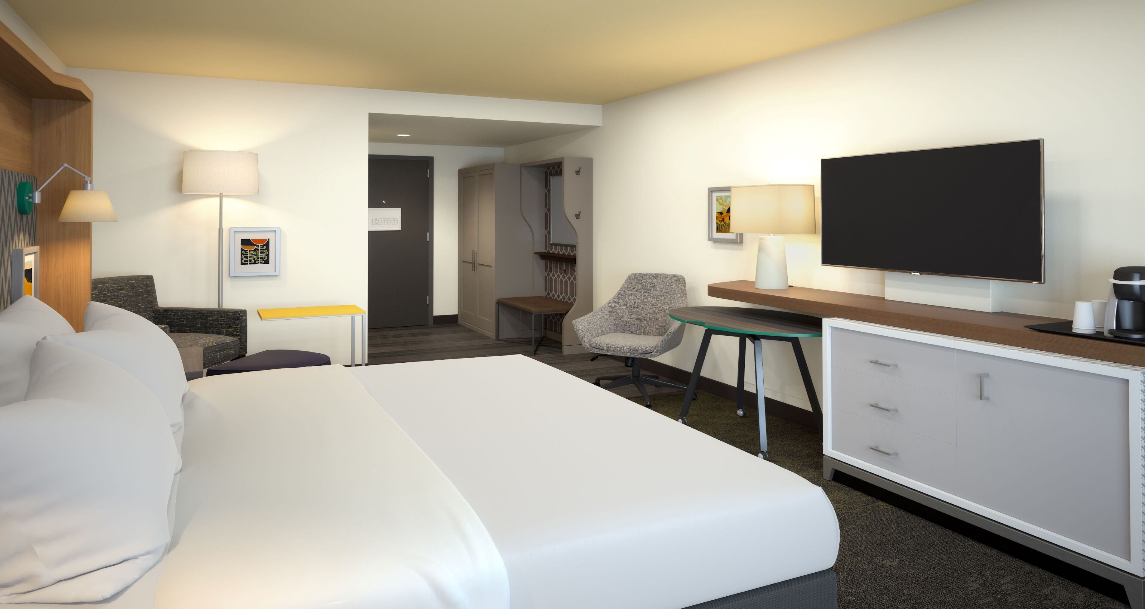 A hotel room with a large bed, a desk with a flat-screen TV, a chair, a lamp, and a wardrobe.