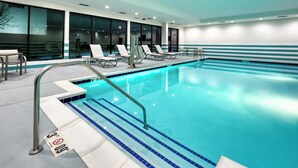 Ein modernes Hallenbad mit klarem, blauem Wasser, einer Metallleiter und mehreren Liegestühlen.