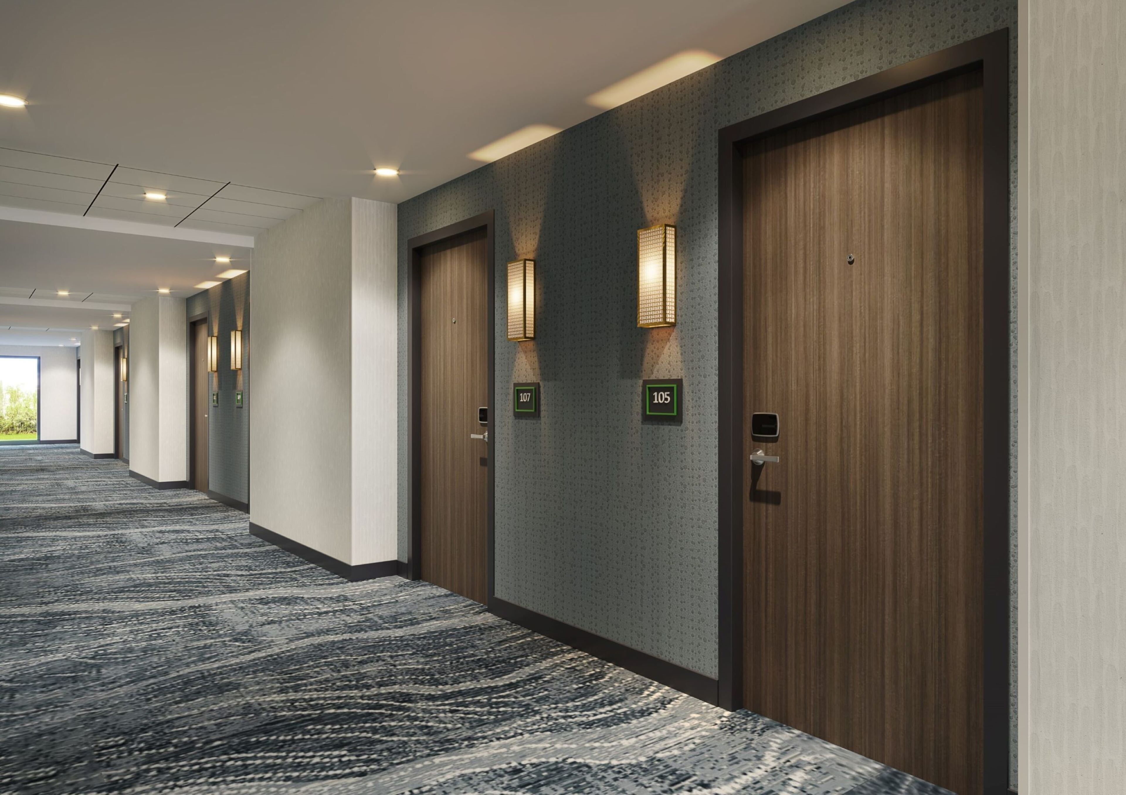 Un pasillo de hotel con piso alfombrado, puertas de madera y luminarias fijadas a la pared.