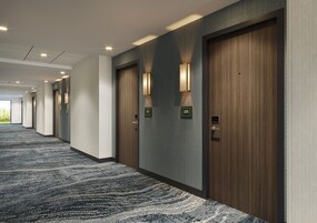 Un couloir d'hôtel avec un revêtement de sol en moquette, des portes en bois et des luminaires fixés au mur.