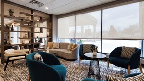 Ein moderner Loungesessel mit einem Ecksofa, zwei Sessel, einem Couchtisch und einem Bücherregal voller dekorativer Gegenstände. Große Fenster bieten einen Blick ins Freie.
