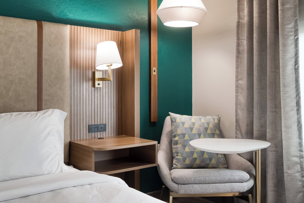 Une chambre d’hôtel comprenant un lit, une table de chevet, une lampe, une chaise et une petite table.
