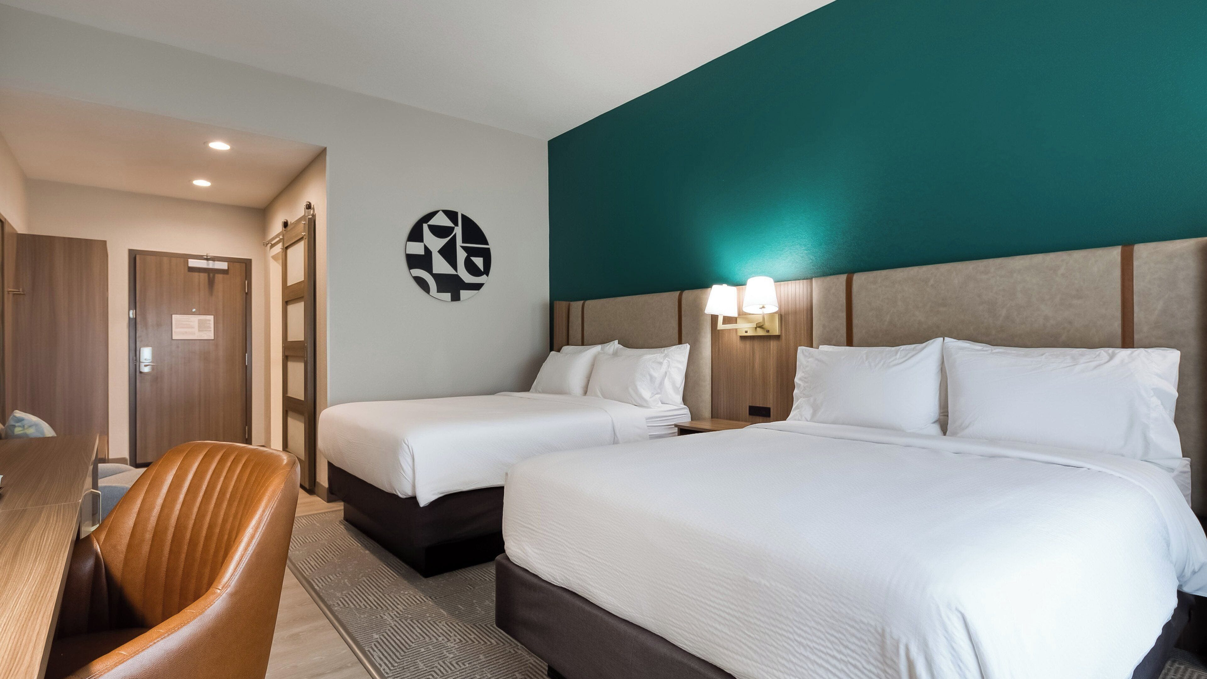 A hotel room with two beds, a desk, and a chair.