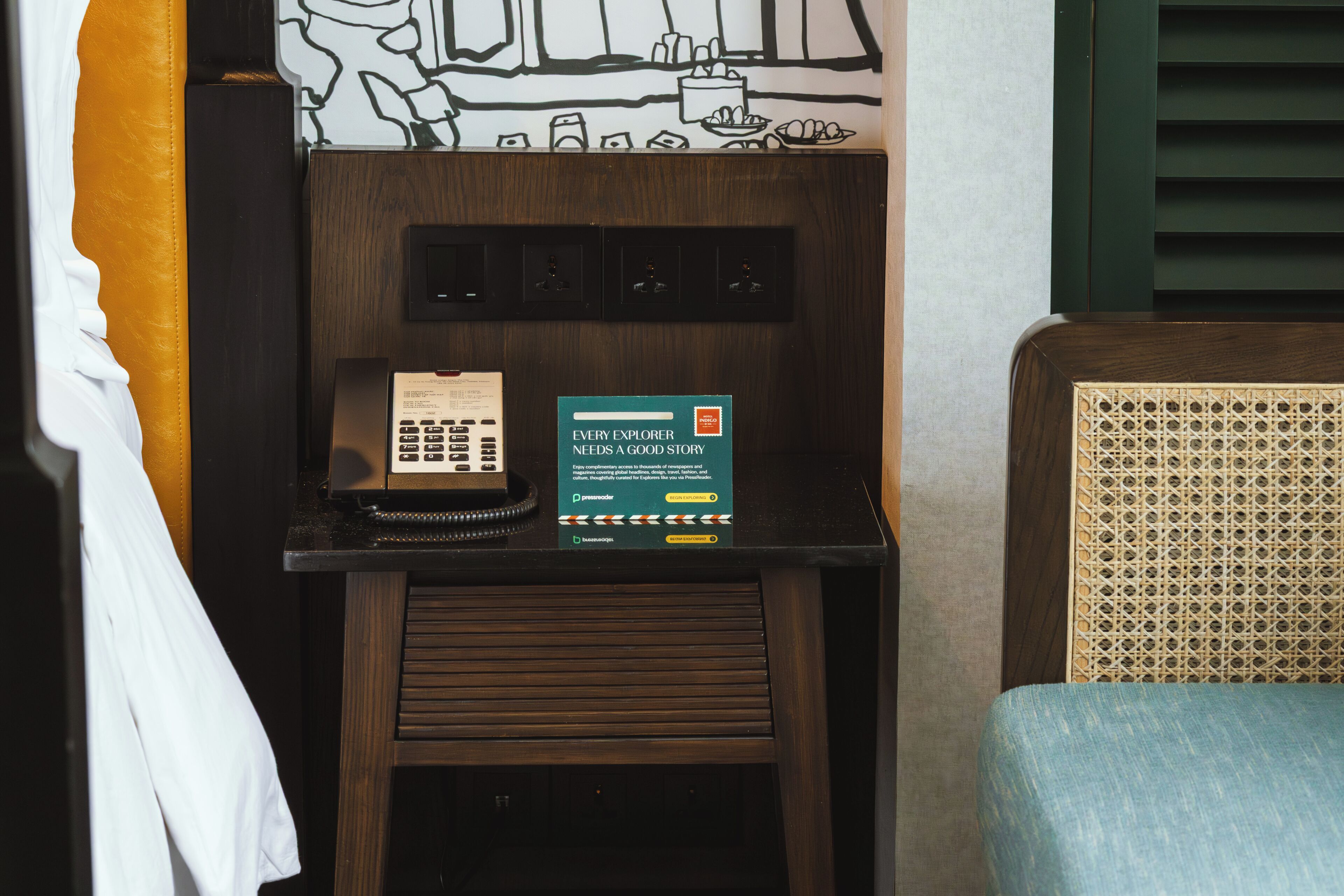 A hotel reception desk with a telephone, a digital display, and a wall art piece.