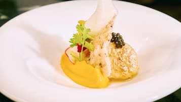 Une assiette blanche avec un morceau de poisson, une sauce jaune et quelques accompagnements.