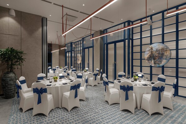 Un salón de conferencias con mesas redondas, sillas blancas con cintas azules y un gran globo decorativo en la pared.