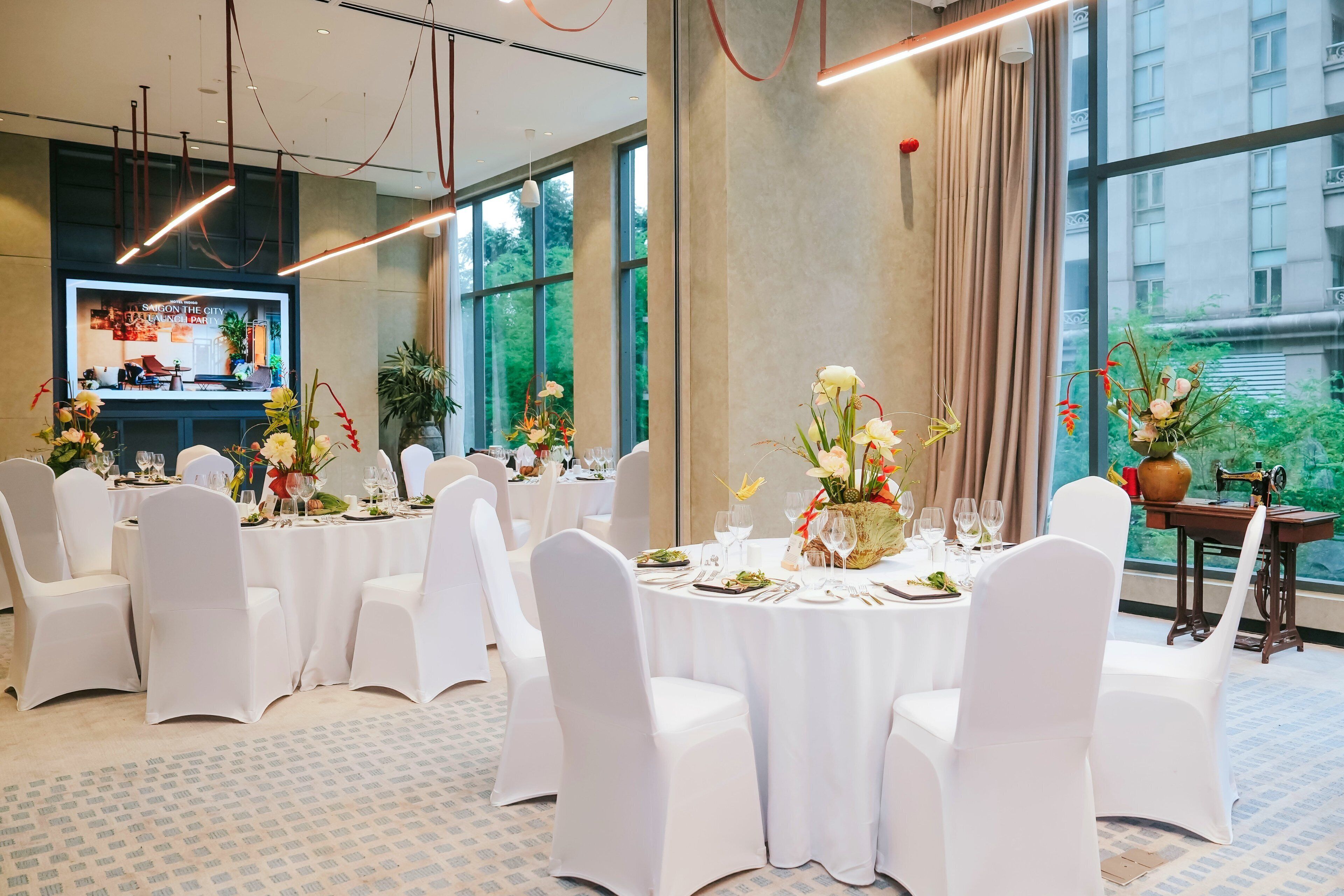 Uma sala de conferências com mesas redondas, cadeiras brancas e centros de mesa com flores.