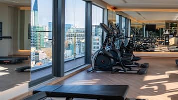 A gym with exercise equipment, large windows, and a city view.