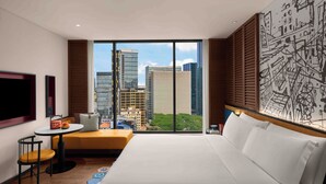 A hotel room with a large bed, a small table with a chair, a sofa, a TV, and a large window with a city view. - Hotel Indigo Saigon The City by IHG (Ho Chi Minh City)