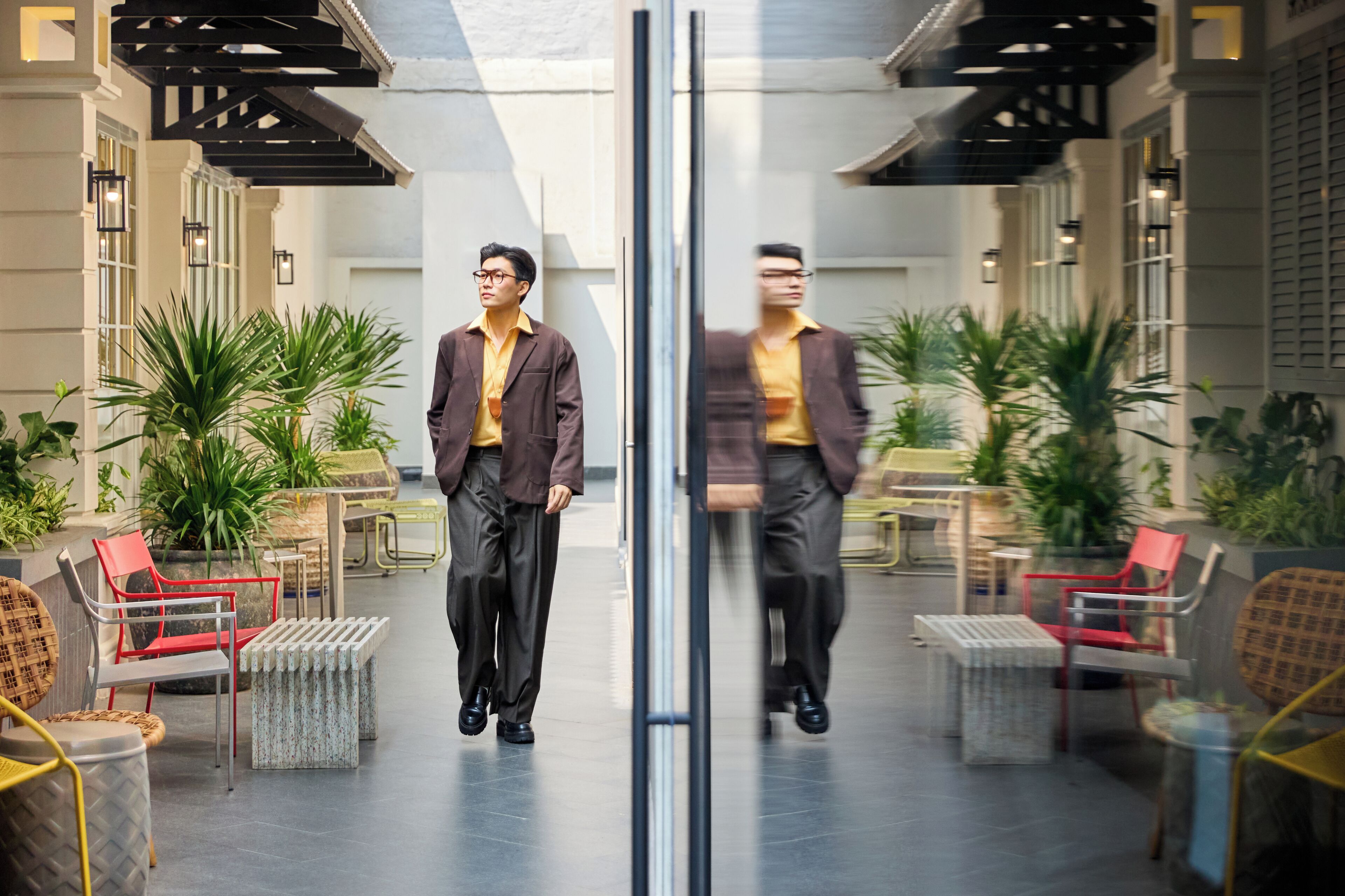Un homme traverse un hall d’entrée moderne, avec des portes en verre, des plantes en pot et des meubles contemporains.