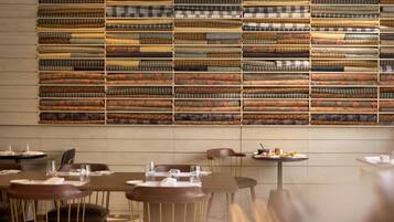 Un restaurant avec des tables et des chaises, un mur recouvert de piles de nappes pliées et un plancher en bois.