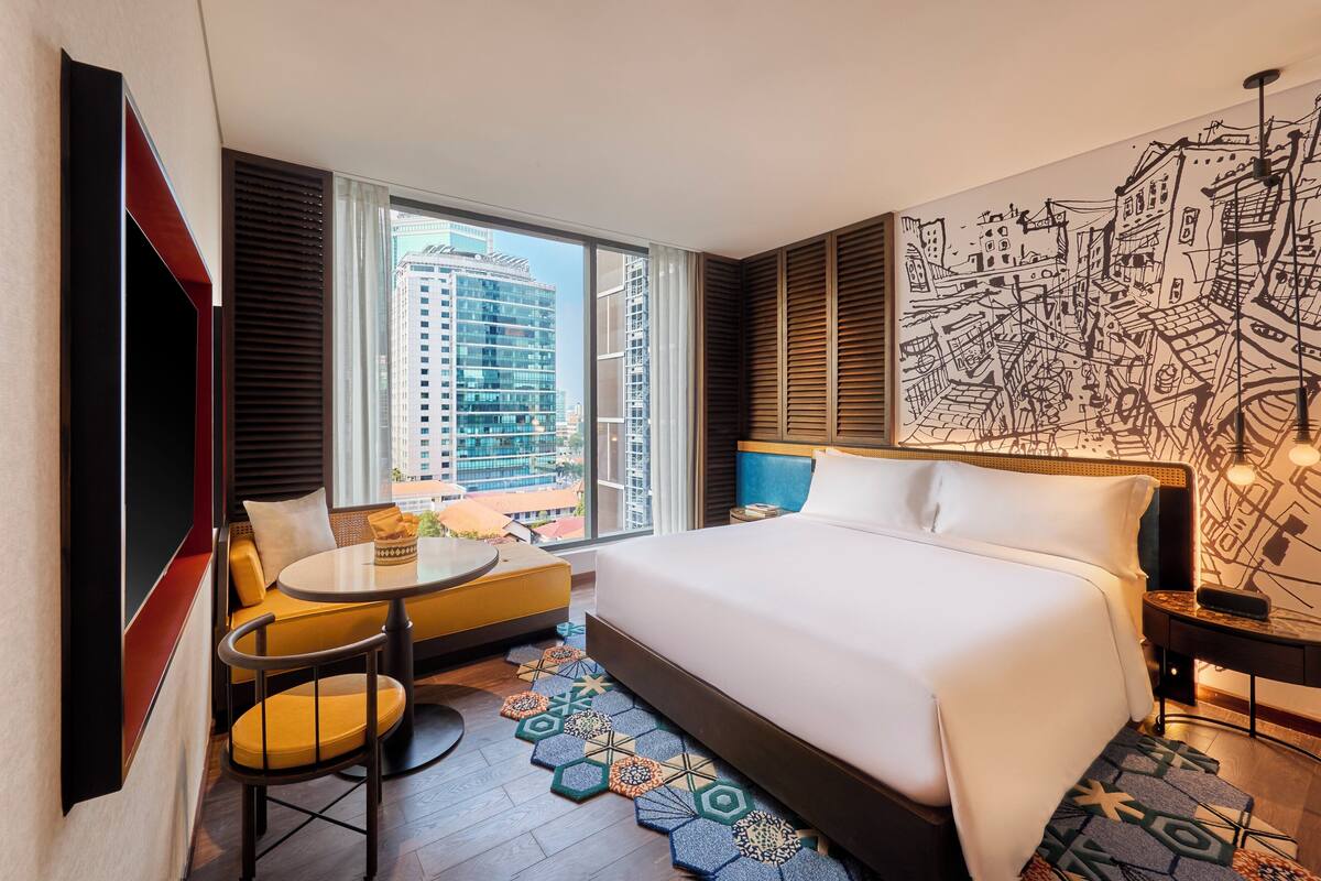 Une chambre d’hôtel avec un grand lit, un canapé, une table ronde et une vue sur le paysage urbain grâce à de grandes fenêtres.