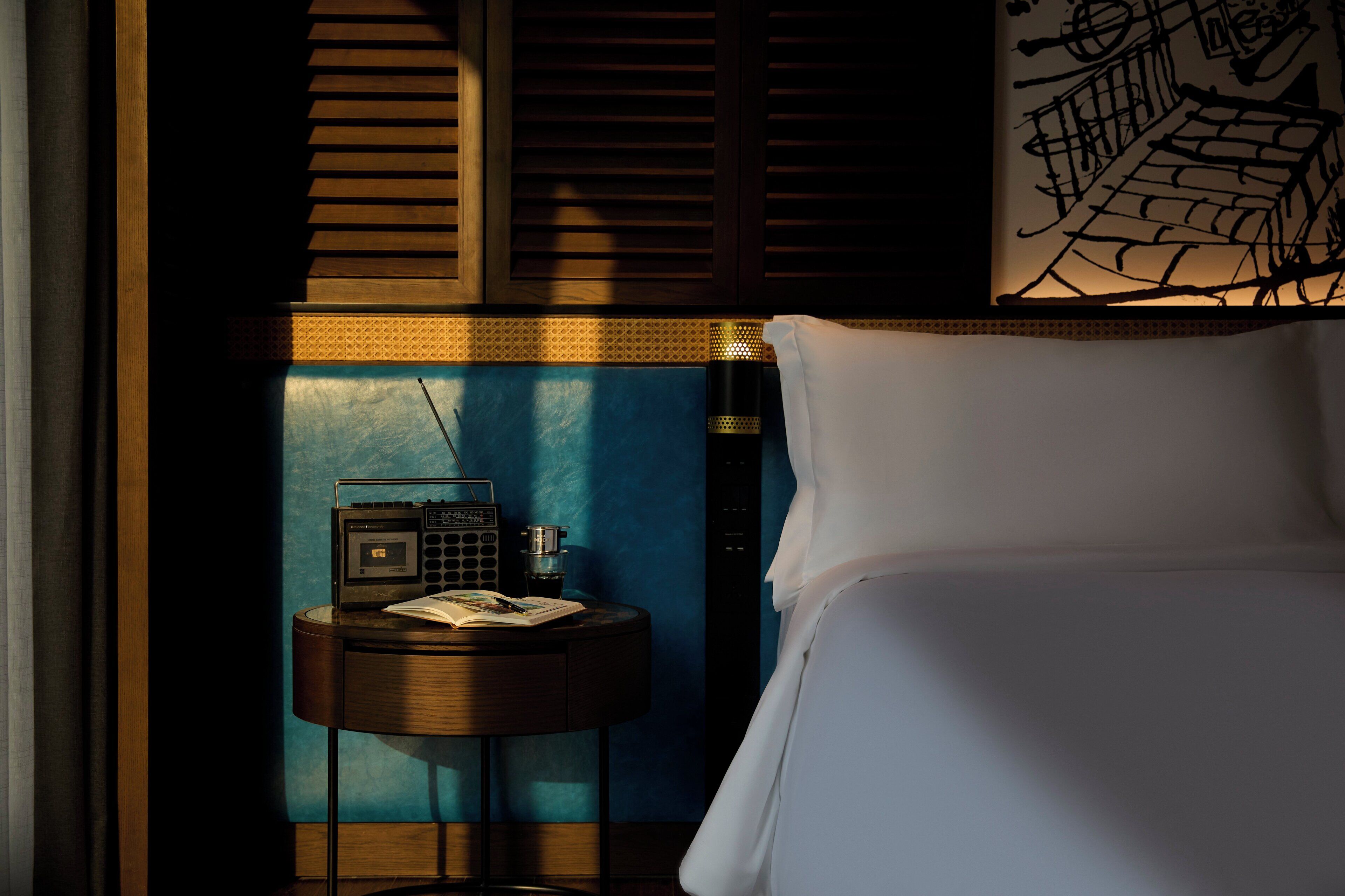 Una camera d'albergo con un letto, un comodino con una radio e una parete con un motivo geometrico.