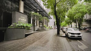 A modern hotel with a glass facade, outdoor seating area, and a tree-lined sidewalk. - Hotel Indigo Saigon The City by IHG (Ho Chi Minh City)