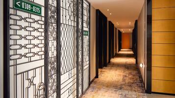 A corridor with patterned metal partitions, directional signs, and a carpeted floor.