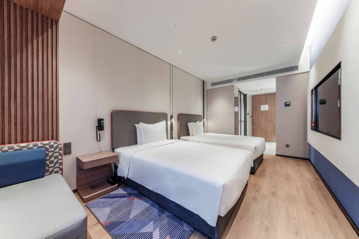 A hotel room with a large bed, a desk, a chair, and a TV.