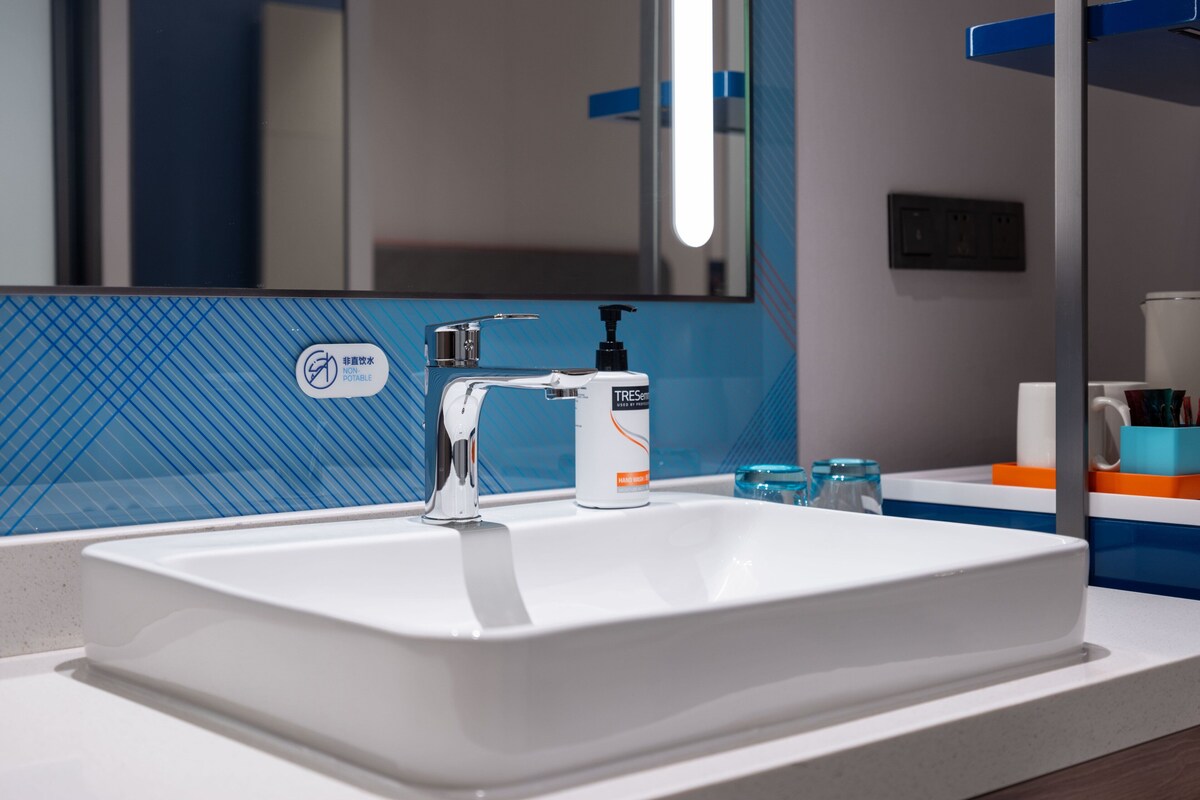 A bathroom with a white sink, a mirror, and a soap dispenser.