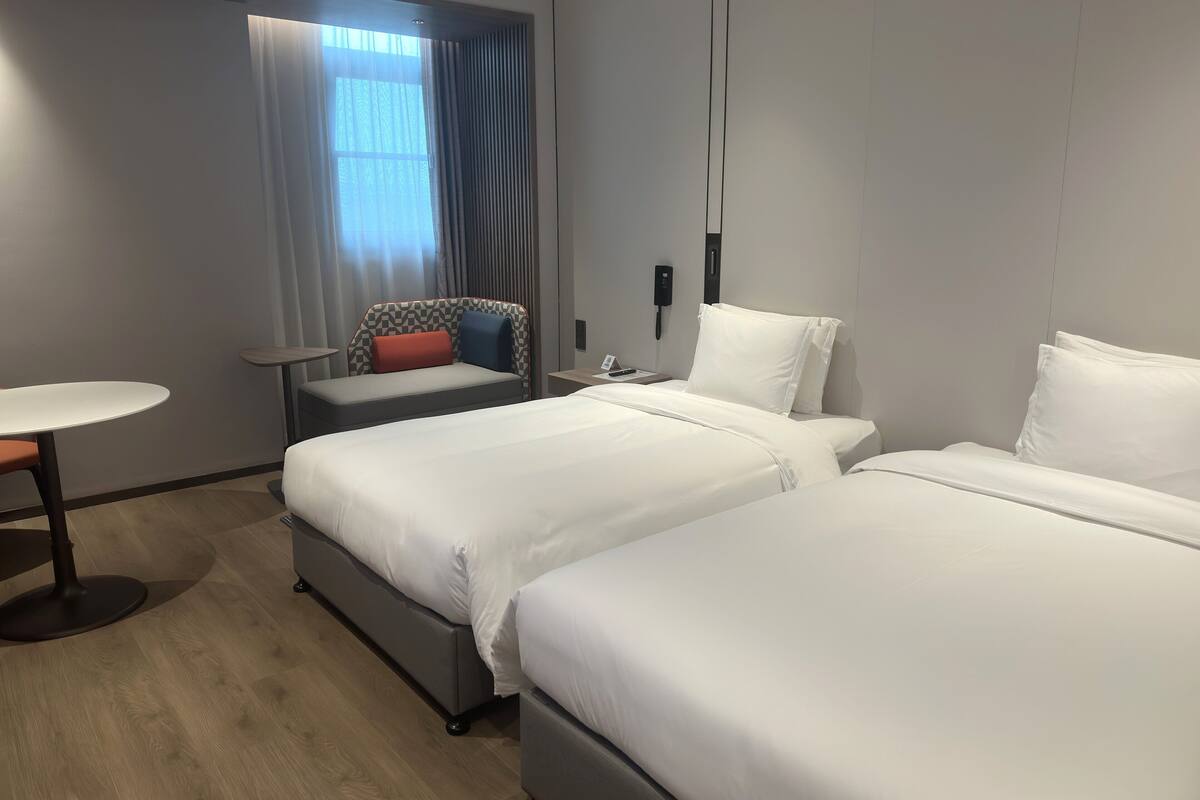 A hotel room with two beds, a small table, and a window with curtains.
