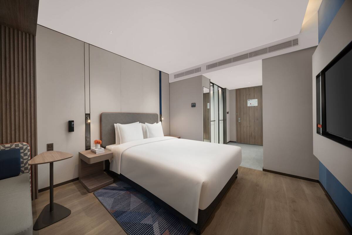 A modern hotel room with a large bed, bedside table, and a TV.