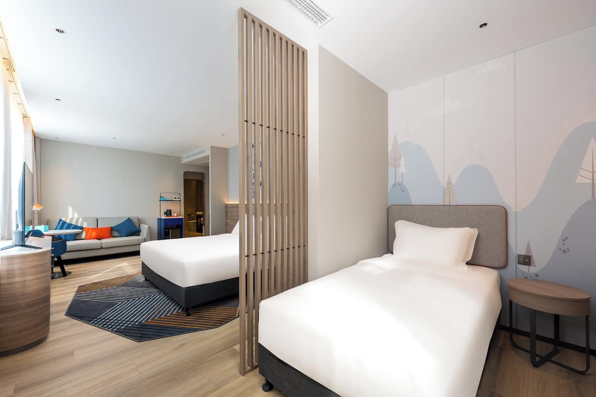 Ein modernes Hotelzimmer mit zwei Betten, einem Schreibtisch und einer Sitzecke.