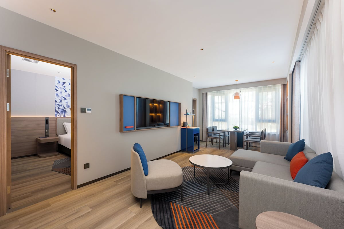 Ein modernes Hotelzimmer mit einer Couch, einem Sessel und einem Essbereich mit Tisch und Stühlen.