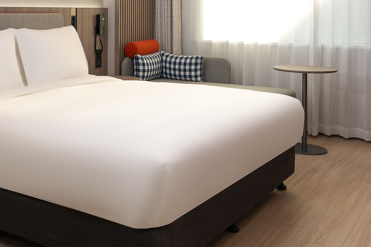 Une chambre d’hôtel avec un grand lit, une table de chevet, une chaise, une petite table ronde et un téléphone.