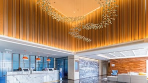 Un hall d’hôtel moderne comprenant un comptoir d’accueil, un espace salon et des éléments décoratifs au plafond.