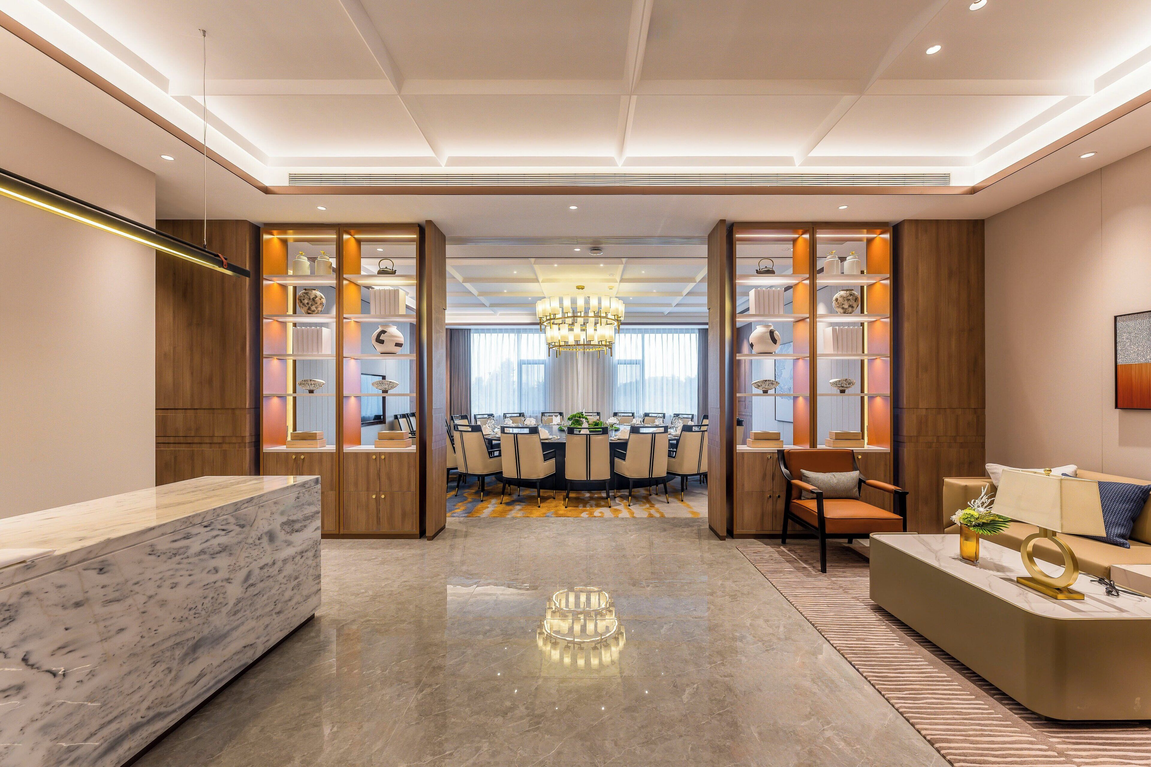 Un hall de hotel con un mostrador de recepción de mármol, un comedor con candelabro y un mostrador de recepción con sofá.