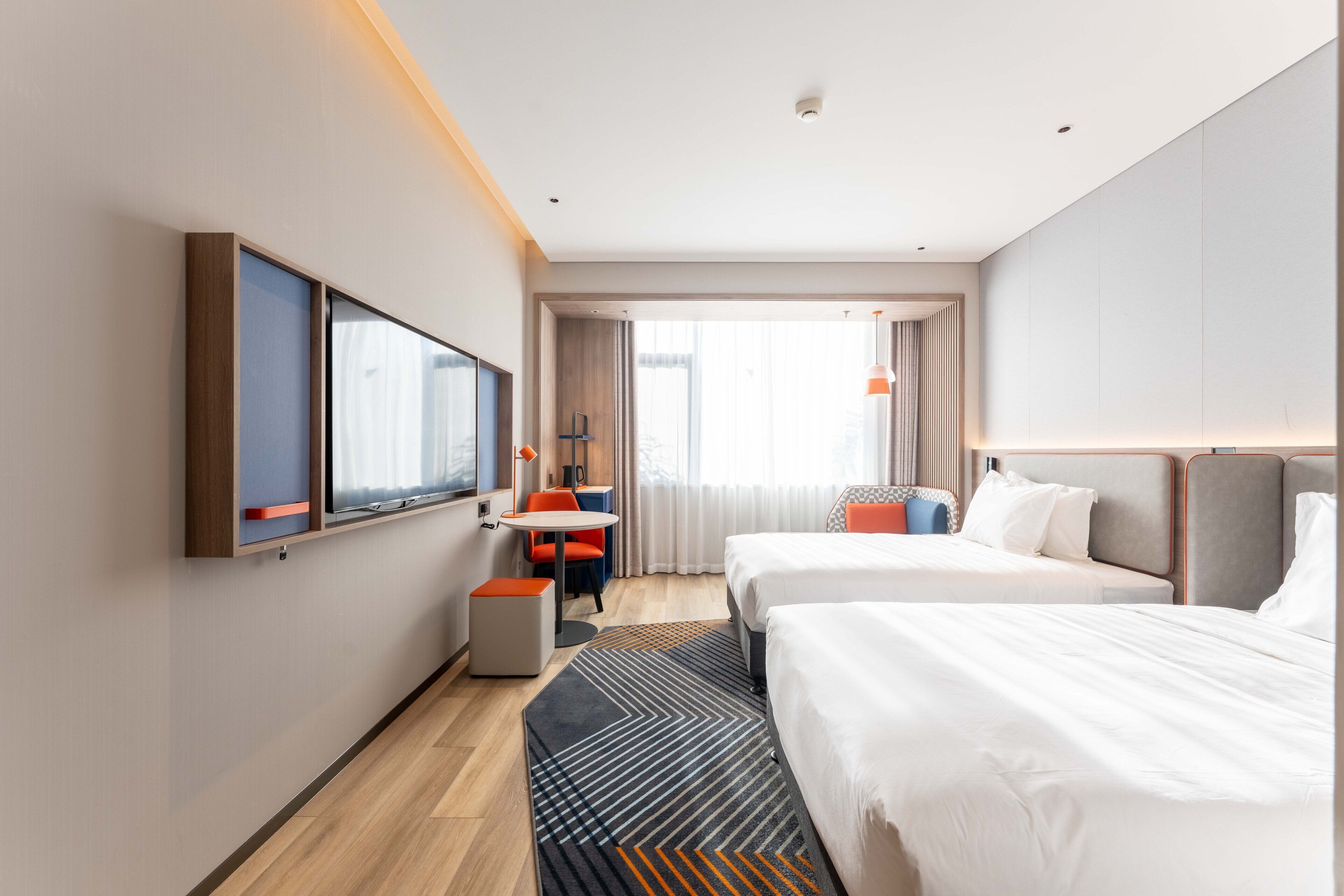 A hotel room with two beds, a desk, a chair, a TV, and a window with curtains.
