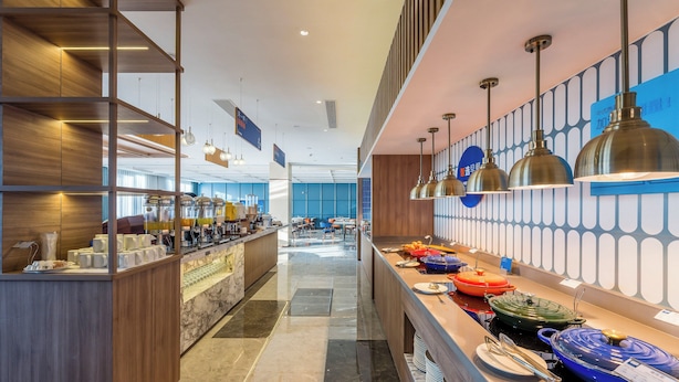 Un hall d’hôtel moderne avec un long comptoir d’accueil, un bar à café et un espace buffet proposant divers plats.