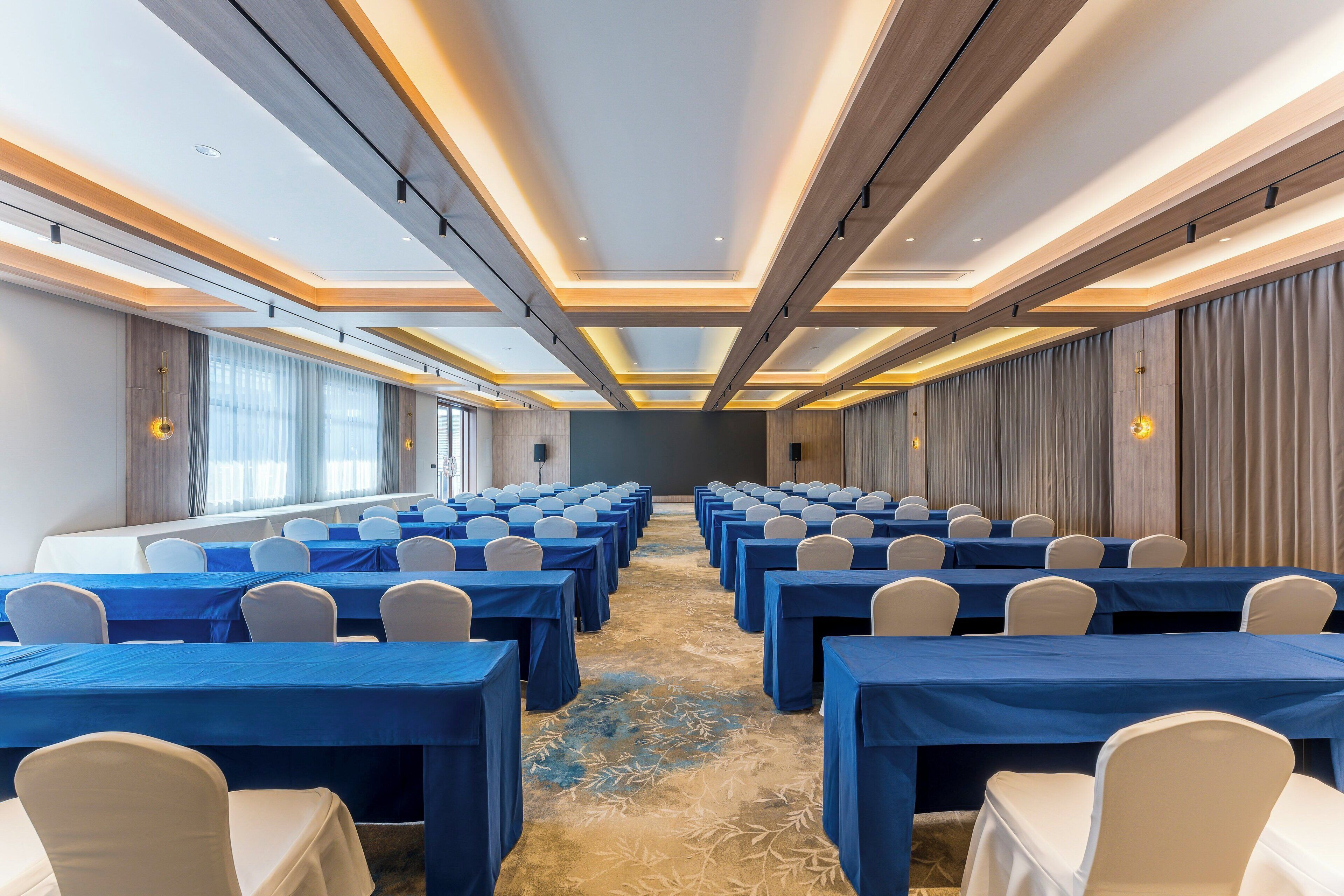 A conference room with rows of tables and chairs, a patterned carpet, and a modern ceiling design.