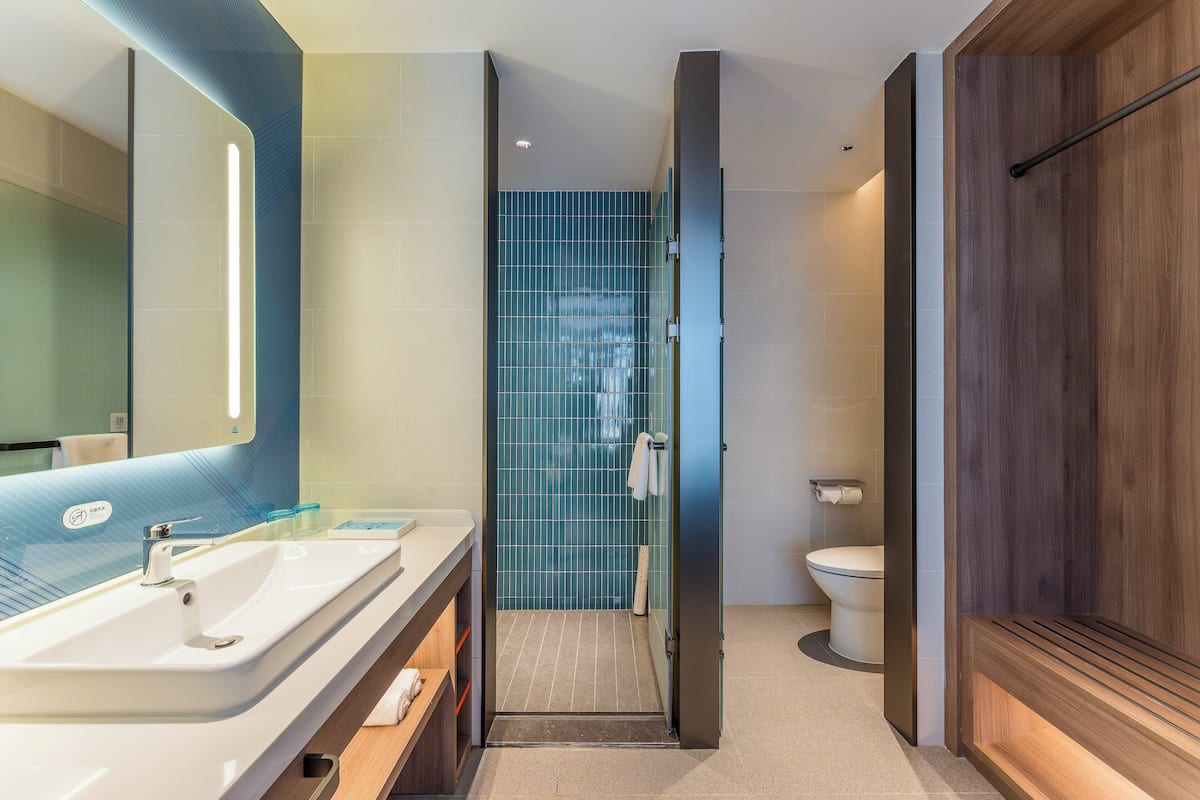 Une salle de bain moderne avec un grand miroir, un lavabo, un espace douche et des toilettes.