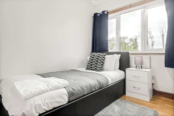 Une chambre à coucher avec un lit, une table de chevet, une lampe et une fenêtre avec des rideaux.