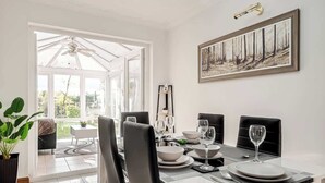 A dining area with a table set for four, a painting on the wall, and a view through a glass door. - 3 Bedroom Home With 2 Bathrooms & Free Parking (Bedford)