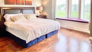 A bedroom with a large bed, a nightstand, a lamp, and a window with a view of the outdoors. - Ravine House, 4000sqf, View, AC,Sleep12+

 (Calgary)